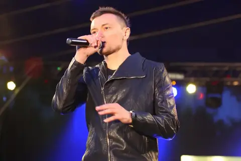 Artysta liber śpiewa do mikrofonu na scenie, ubrany w czarną kurtkę.