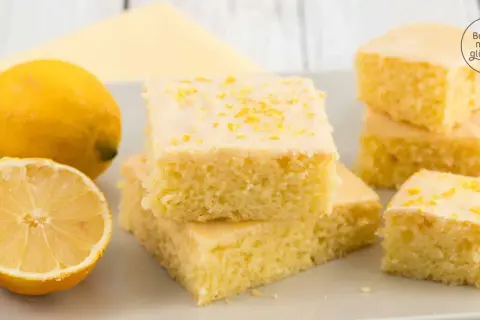 Saftiger Zitronenkuchen vom Blech, bestreut mit Zitronenschale. Daneben liegen frische Zitronen.