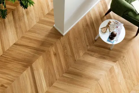 Un elegante parquet a spina di pesce, con un tavolino bianco e una poltrona verde. Per mantenere la sua bellezza, chiediti ogni quanto lavare il parquet.