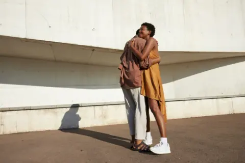 Ein Paar umarmt sich innig vor einer Betonwand. Ihre Körperhaltung strahlt tiefe **liebe und vertrauen** aus, ein Moment der Verbundenheit im hellen Sonnenlicht.