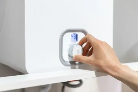Mano che gira la manopola per spegnere la caldaia a condensazione. Display digitale mostra 48°C.