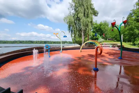 Kolorowy plac zabaw wodnych przy Jeziorze Paprocany, z fontannami i tęczą, zaprasza do zabawy w upalny dzień.