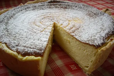 Une délicieuse tarte au fromage blanc, saupoudrée de sucre glace, prête à être dégustée sur une nappe à carreaux rouges.