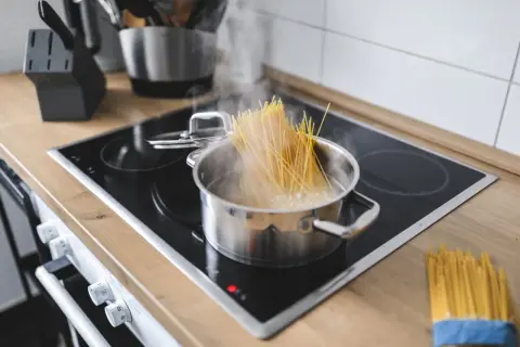 Spaghetti kochen in einem Topf auf dem Herd. Ein Bündel Spaghetti liegt daneben. Der Trick, wie viel Spaghetti pro Person, ist hier visuell dargestellt.