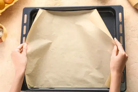 Ręce układają papier do pieczenia na blasze. Zastanawiasz się, czym zastąpić papier do pieczenia?