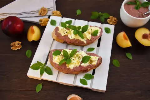 Zwei Bruschettas mit Pflaumenaufstrich, Käse und Basilikum, garniert mit Walnüssen und frischen Pflaumen.