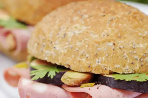 Un délicieux sandwich mortadelle garni de tranches d'aubergine, de pistaches et de persil frais, prêt à être dégusté.