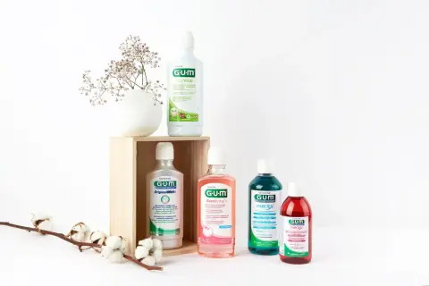 Zestaw płynów do płukania jamy ustnej GUM, w tym ActiVital, Original White, SensiVital+ i Paroex, obok delikatnych kwiatów.