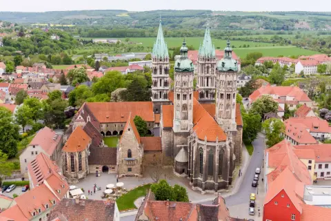 Der Naumburger Dom, ein Meisterwerk romanischer Architektur, thront über der Stadt. Seine Türme ragen in den Himmel, umgeben von roten Dächern und grünen Hügeln.
