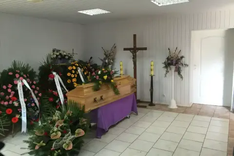 Drewniana trumna otoczona wieńcami i kwiatami, krzyż i świece tworzą najpiękniejsze ostatnie pożegnanie.