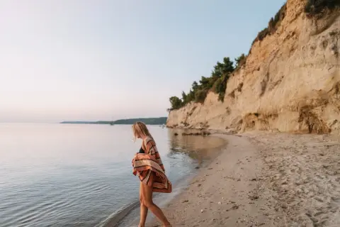Mujer rubia camina por la playa, sintiendo la brisa marina. Ella anhela la libertad y el deseo de querer viajar sola.