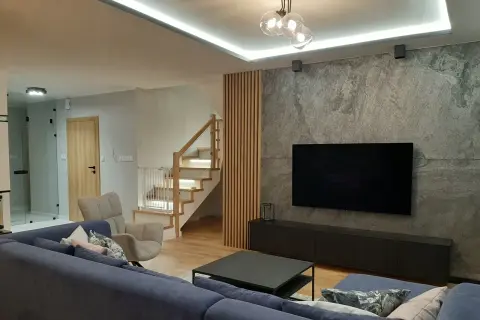 Nowoczesne lamele ścienne aranżacje tworzą ciepłą atmosferę obok kamiennej ściany z TV.