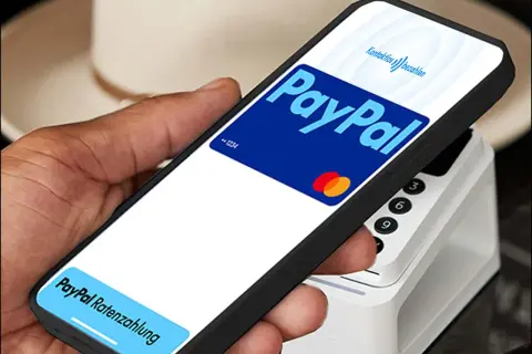 Hand hält Smartphone mit PayPal-Logo und "Kontaktlos bezahlen" für eine schnelle Transaktion. Unten: "PayPal Ratenzahlung".