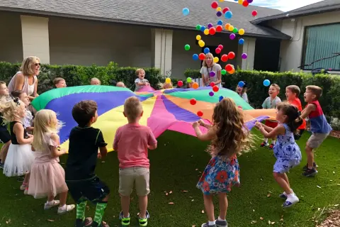 Children joyfully engage in gross motor activities for toddlers, tossing colorful balloons into the air while holding a large parachute.