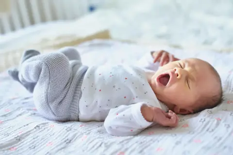 Ein Baby gähnt auf einer Decke mit Sternen. Wann Babys alleine einschlafen, ist eine Frage, die viele Eltern beschäftigt.