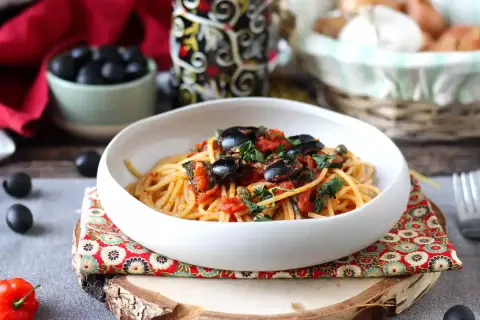 En skål med spaghetti puttanesca, toppad med svarta oliver och persilja. Ett härligt recept för en smakrik middag.