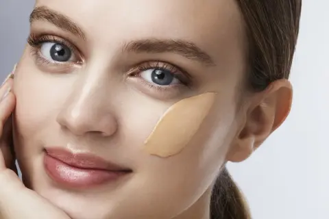 Una donna con un tocco di fondotinta sulla guancia, un esempio visivo di come applicare il fondotinta per un look naturale.