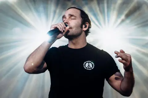Sänger mit geschlossenen Augen und Mikrofon, der seinen erfolgreichsten Song aller Zeiten performt.