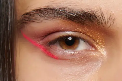 Occhio con eyeliner fucsia audace e ombretto dorato scintillante. Un look di trucchi per gli occhi che cattura l'attenzione.