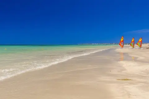 Piękna plaża w Tunezji w czerwcu. Idealna pogoda na windsurfing, trzy kolorowe żagle czekają na wiatr.