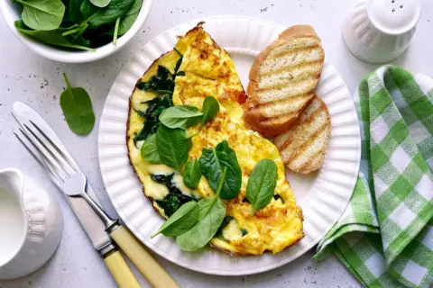 Pyszny omlet ze szpinakiem, podany z grzankami i świeżymi liśćmi szpinaku. Idealny na zdrowe śniadanie.