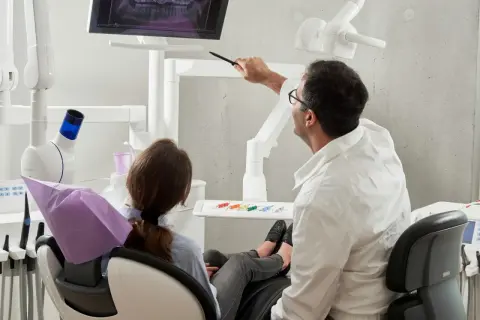 Dentysta omawia z pacjentką zdjęcie RTG, wyjaśniając przebieg leczenia. Ciekawe, ile zarabia dentysta za taką troskę o zdrowie pacjentów.