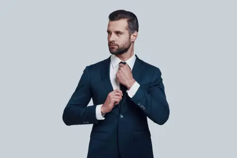 Elegancki mężczyzna w granatowym garniturze poprawia krawat. Idealna biała koszula do granatowego garnituru.