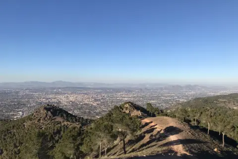 Vista panorámica desde la sierra de carrascoy, con un extenso paisaje urbano y montañas al fondo bajo un cielo azul despejado.