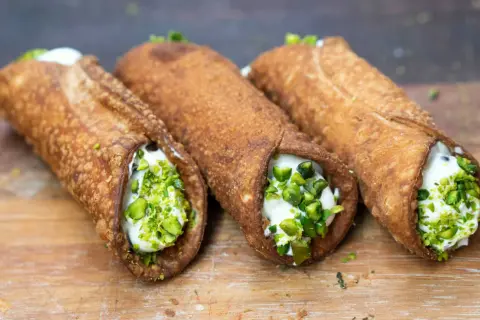 Trzy chrupiące cannoli, jedne z najpopularniejszych dań włoskich, wypełnione kremem i posypane pistacjami.
