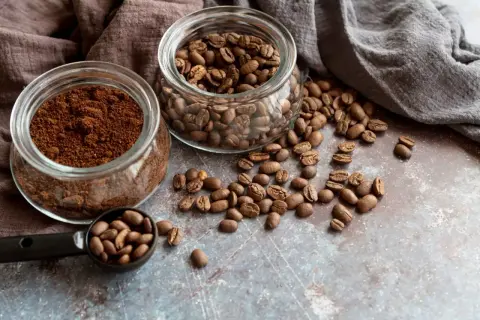 Due barattoli di vetro, uno con caffè macinato e l'altro con caffè in grani, con chicchi sparsi. Quale scegliere per il tuo caffè perfetto?
