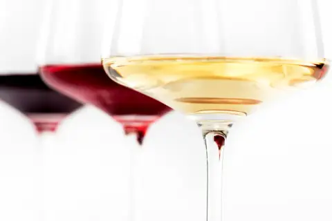 Trzy kieliszki z winem: ciemnoczerwonym, rubinowym i białym. Wino się pieni, tworząc subtelne refleksy.