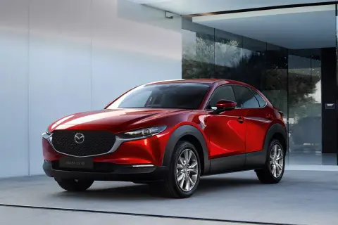 Elegancka, czerwona Mazda CX-30 błyszczy przed nowoczesnym budynkiem z dużymi oknami.