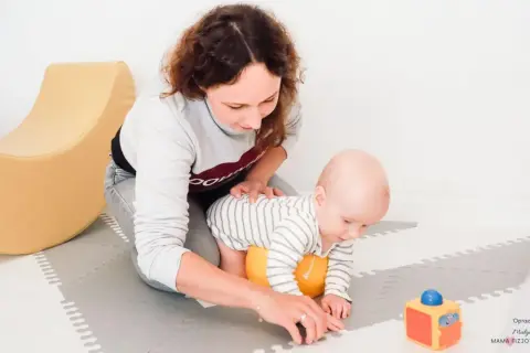 Mama wspiera roczne dziecko w nauce raczkowania. Radosne zabawy z maluszkiem na macie.