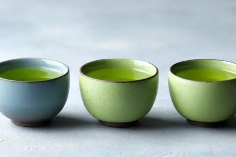 Trois tasses de thé vert vif, une bleue et deux vertes, suggérant la dose maximale de thé vert par jour pour une dégustation paisible.