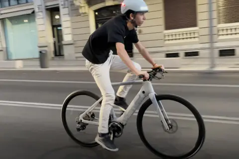 Un joven con casco y ropa casual pedalea una bicicleta eléctrica por la ciudad.