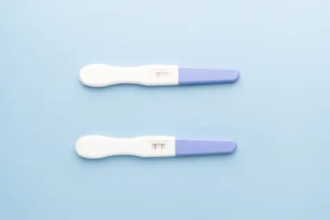 Dwa testy ciążowe na jasnoniebieskim tle. Jeden pokazuje jeden pasek, drugi dwa. Kiedy zrobić test ciążowy?