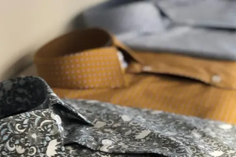 Dettaglio di camicie con fantasie diverse. Una grigia floreale, una senape a pois e una azzurra. Perfette per ogni occasione, con un fermamaniche camicia per un tocco di stile.