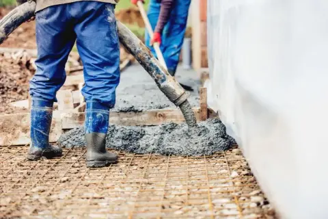 Pracownicy wylewają beton na zbrojenie. Sprawdź aktualny suchy beton cena 1m3.