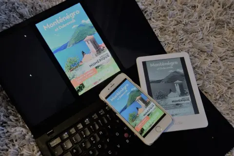 Un ordinateur portable, un smartphone et un **kindle audio** affichent un guide numérique sur le Monténégro et Dubrovnik.
