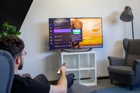 Mężczyzna siedzi w fotelu i ogląda telewizor z menu ustawień obrazu.