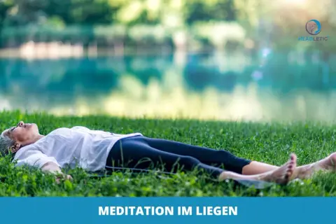 Frau genießt eine friedliche Meditation im Liegen auf einer grünen Wiese am See.