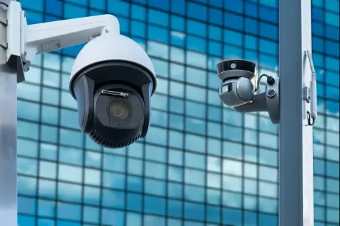 Deux caméras de vidéosurveillance entreprise montées sur un poteau, avec un bâtiment moderne en arrière-plan.