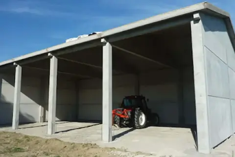 Capannone prefabbricato in cemento in zona agricola, ideale per chi vuole costruire in zona agricola senza essere imprenditore agricolo. Un trattore è parcheggiato all'interno.
