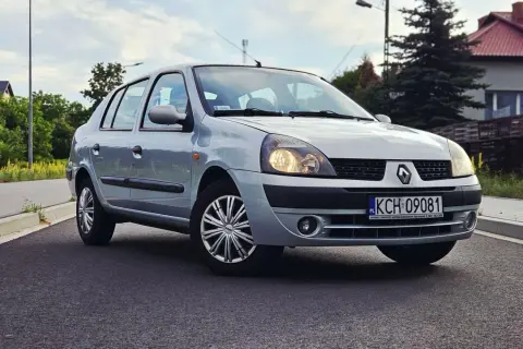 Srebrny Renault Thalia 1.4 z polskimi tablicami rejestracyjnymi KCH 09081 zaparkowany na poboczu drogi.