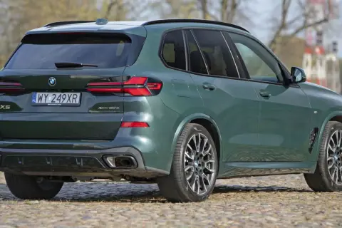 Zielony x5 BMW z napisem XDrive 50e na klapie bagażnika, zaparkowany na bruku.