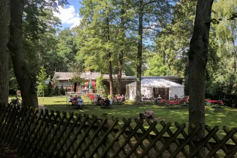 Ein Biergarten im Grünen, mit Gästen an Tischen unter Bäumen und einem Festzelt. Hier findet man **hanffs ruh**.