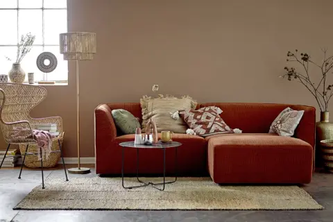 Przytulny salon w stylu boho. Pomarańczowa kanapa, wiklinowy fotel i dywan tworzą ciepłą paletę kolorów ziemi.