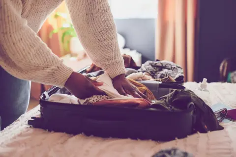 Person packt Kleidung in einen Koffer für den Urlaub. Die Packliste für den Urlaub ist fast komplett.