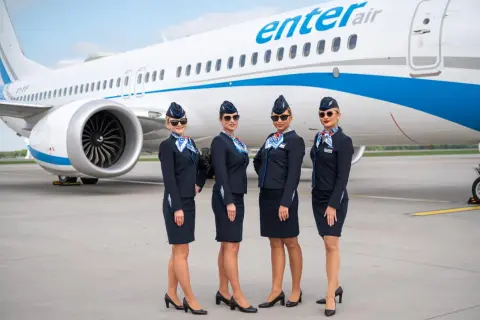 Cztery stewardessy Enter Air w granatowych mundurkach pozują przed samolotem. Czekają, by serwować pyszne jedzenie w przestworzach.