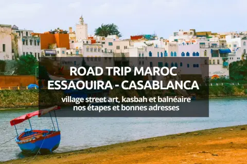 Bateau coloré sur la rive d'une ville côtière marocaine, avec des bâtiments blancs et bleus en arrière-plan.